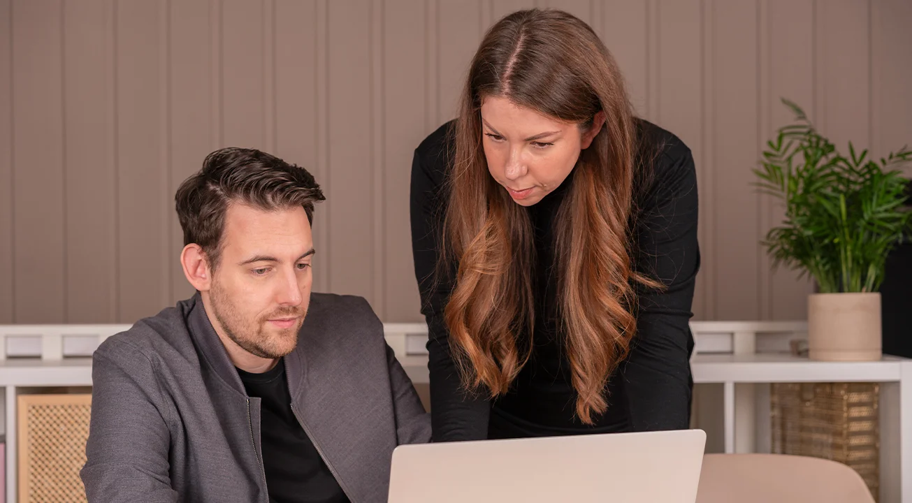 Bence Székely og Orsi Imreh jobber med et markedsføringsprosjekt på en laptop i et moderne kontormiljø.